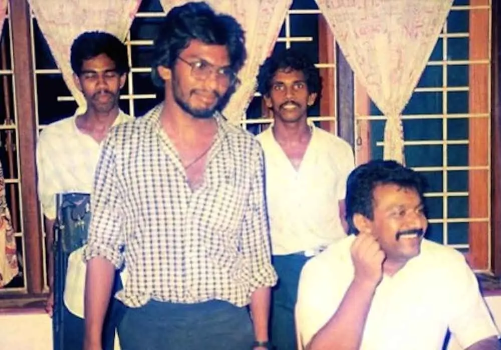 Thileepan debout, lunettes et chemise à carreaux, à côté de Velupillai Prabhakaran assis.